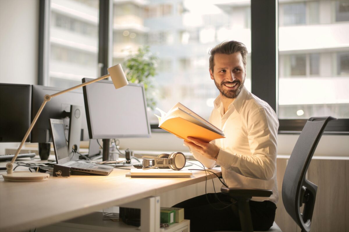 Webseitenentwicklung - Mann sitzt am Arbeitsplatz mit Laptop und Buch